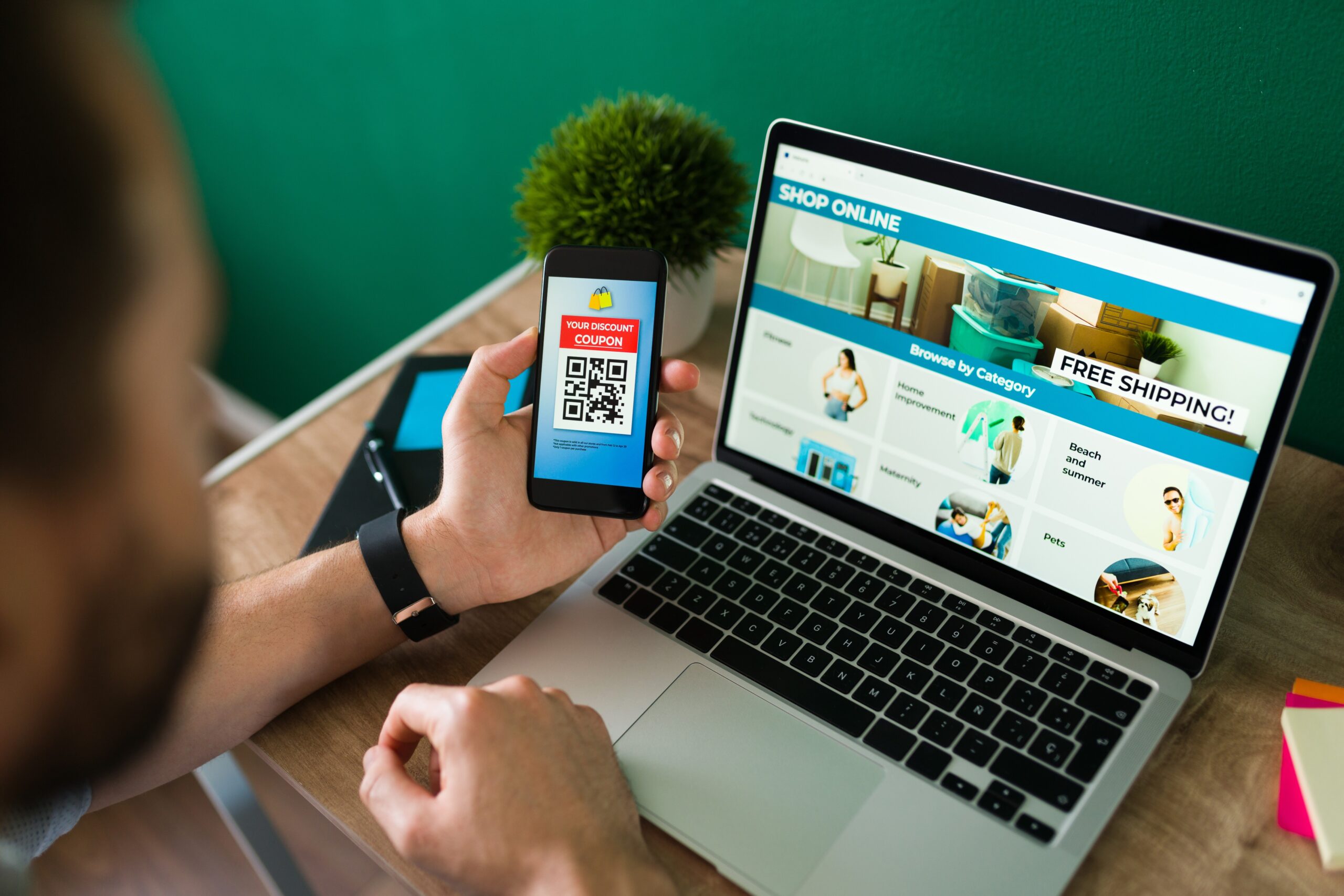 young-man-using-discount-coupon-his-smartphone-some-online-shopping-laptop (1)